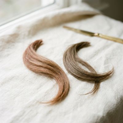 Duas mechas de cabelo castanho lado a lado sobre linho natural, uma com reflexo alaranjado e outra fria e neutra, com luz suave do dia