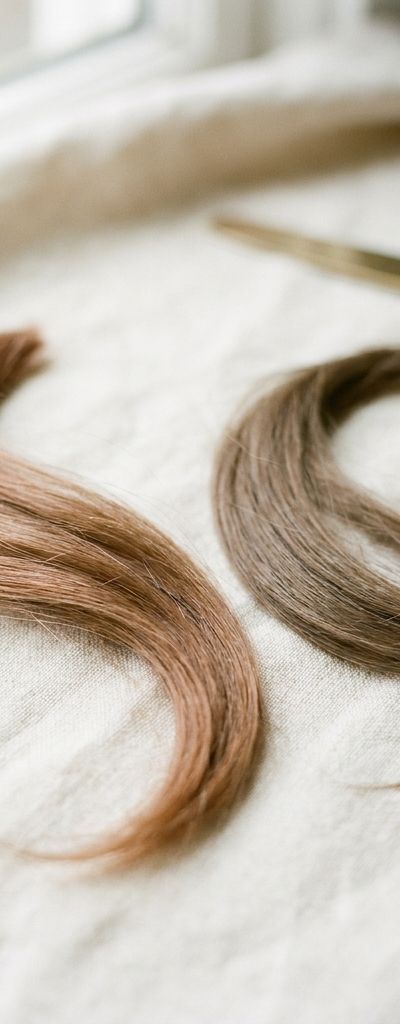 Two locks of brown hair side by side on natural linen, one with an orange cast and one cool and neutral, in soft daylight