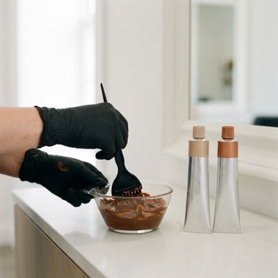 Professional colorist applying Igora Royal to gray roots next to a bowl with the shade-and-natural mix