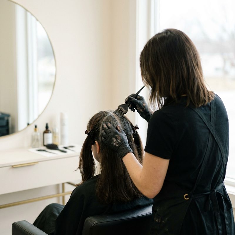 Colorista aplicando a mistura de Igora Royal com pincel na raiz com fios brancos, cabelo preso com grampos de seção