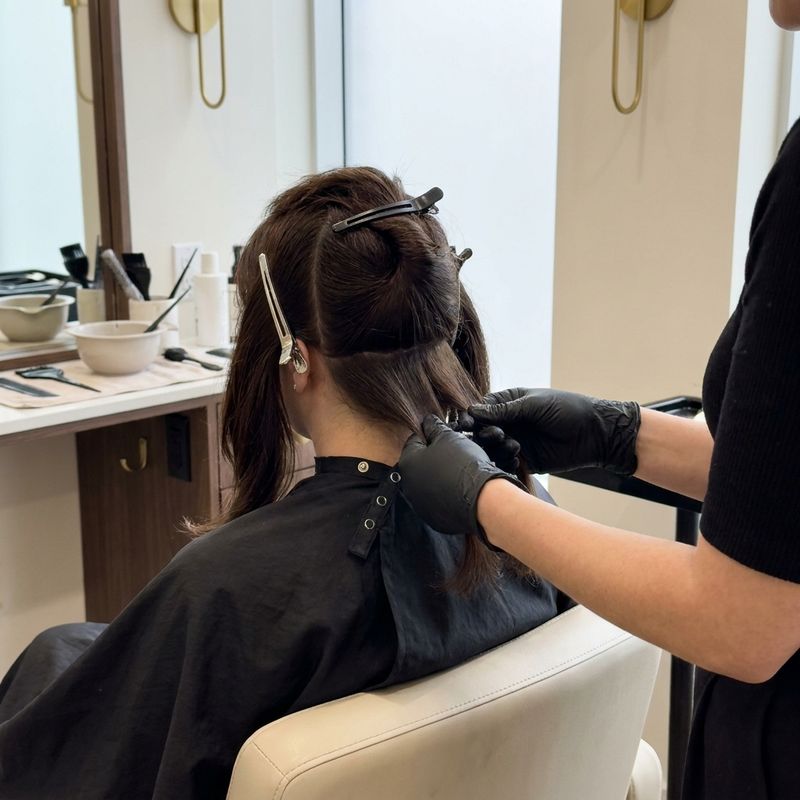 Colorist sectioning a client's hair from behind with clips, preparing clean quadrants before applying bleach in the salon
