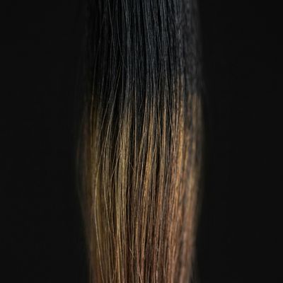 Mecha de cabelo sobre fundo preto mostrando o subjacente quente que aflora por região ao clarear um preto de caixa acumulado, com paleta dourada e cobre