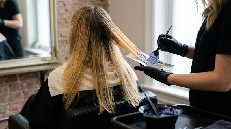 Teste de mecha no trecho clareado de um balayage crescido: neutralizador azul-violeta em uma única mecha de fundo quente, abaixo de uma raiz natural mais escura