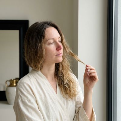 Pessoa observando o próprio cabelo contra a luz de uma janela, comparando o aspecto da raiz e das pontas depois do verão