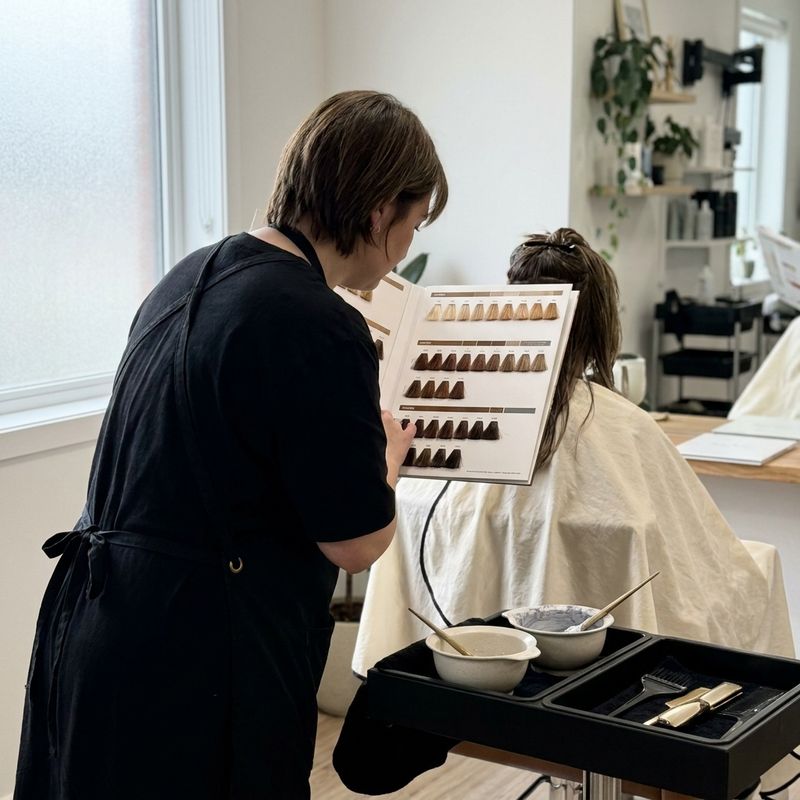 Colorista de espaldas consultando una carta física de muestras de color junto a una clienta sentada, en una cabina de peluquería real