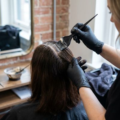 Vista de trás de um cabelo castanho com a raiz recém-retocada mostrando diferença de tom em relação ao comprimento, em um salão com luz natural