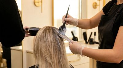 Colorista profissional aplicando toner acinzentado em cabelo loiro para eliminar tons laranjas
