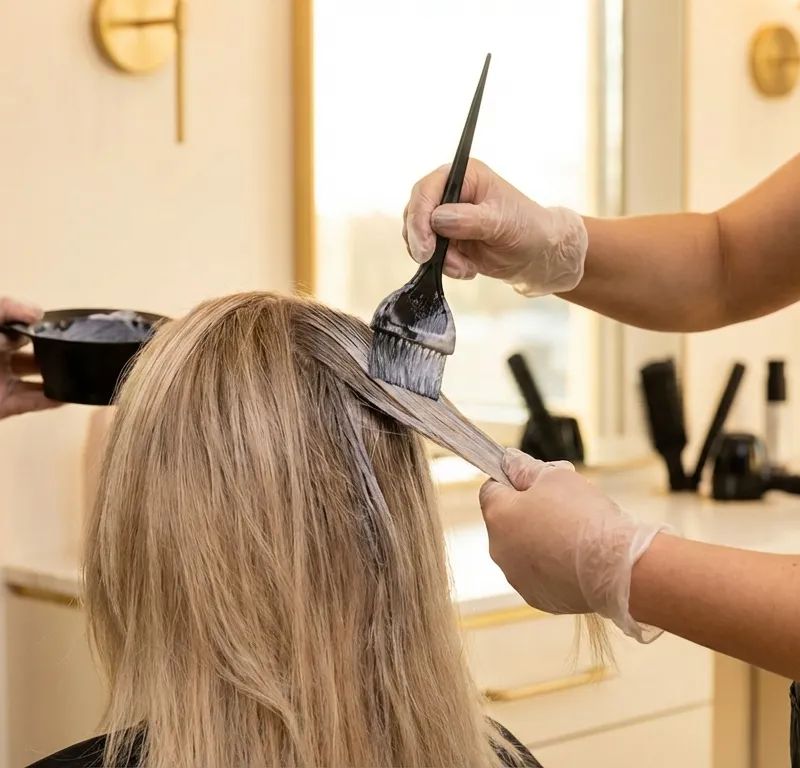 Professional colorist applying ash toner to blonde hair to eliminate orange tones