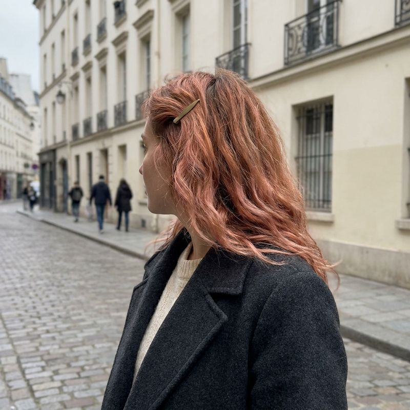 Cabelo cobre morango com matiz rosado juvenil e ondas, visto de perfil numa rua com prédios ao fundo