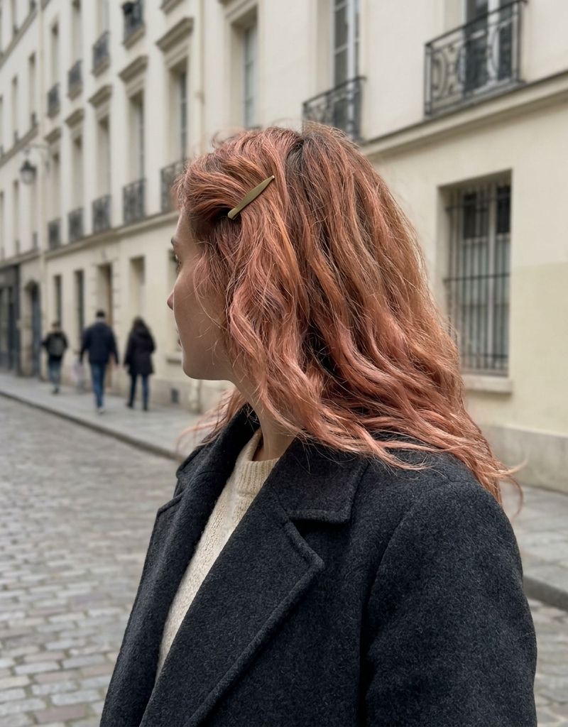 Melena cobre fresa con matiz rosado juvenil y ondas, vista de perfil en una calle con edificios de fondo