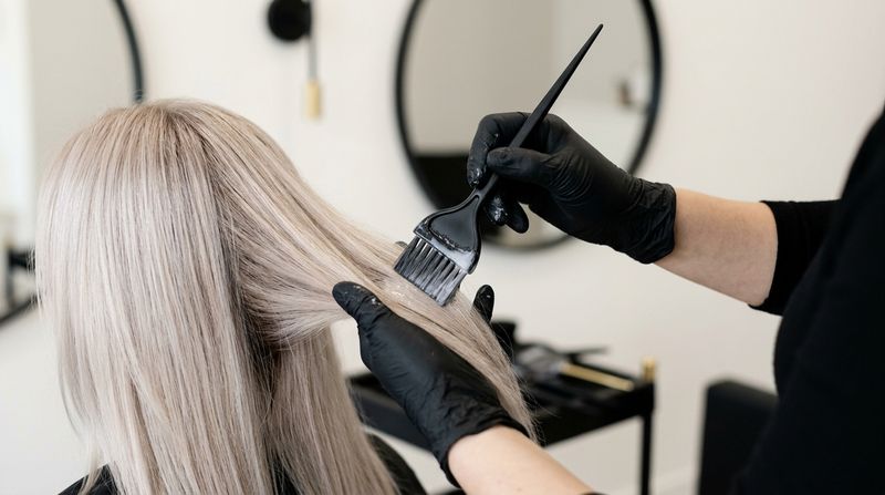 Profesional aplicando un gloss de recarga de bajo volumen sobre cabello rubio perla