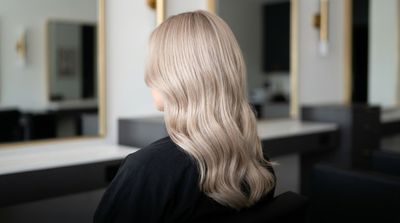 Cabelo velvet blonde acetinado em tom champanhe pérola, fotografado de costas em salão premium com luz lateral suave